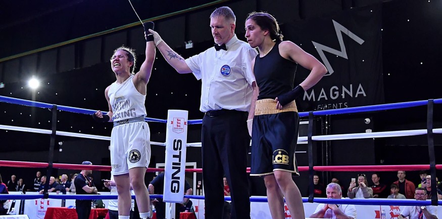 A boxing referee raises Rhea Kanu's left arm aloft in the centre of a boxing ring.